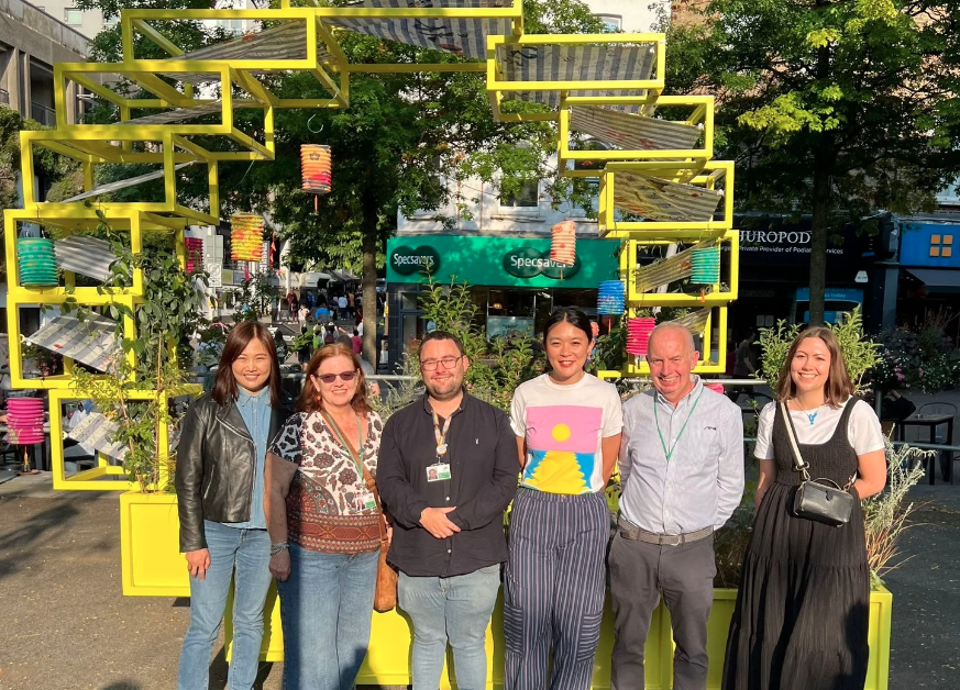 Council Leader Barry Lewis and Councillor Jake Short standing in Sutton High Street in front of the Moon Gate structure with an LBS employee and two women