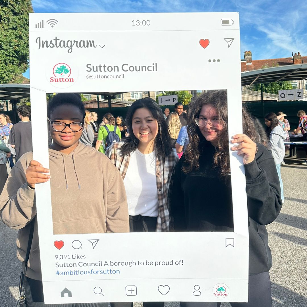 Cheam High students celebrating their exam results. Image shows three smiling young ladies standing behind a giant Instagram photo frame